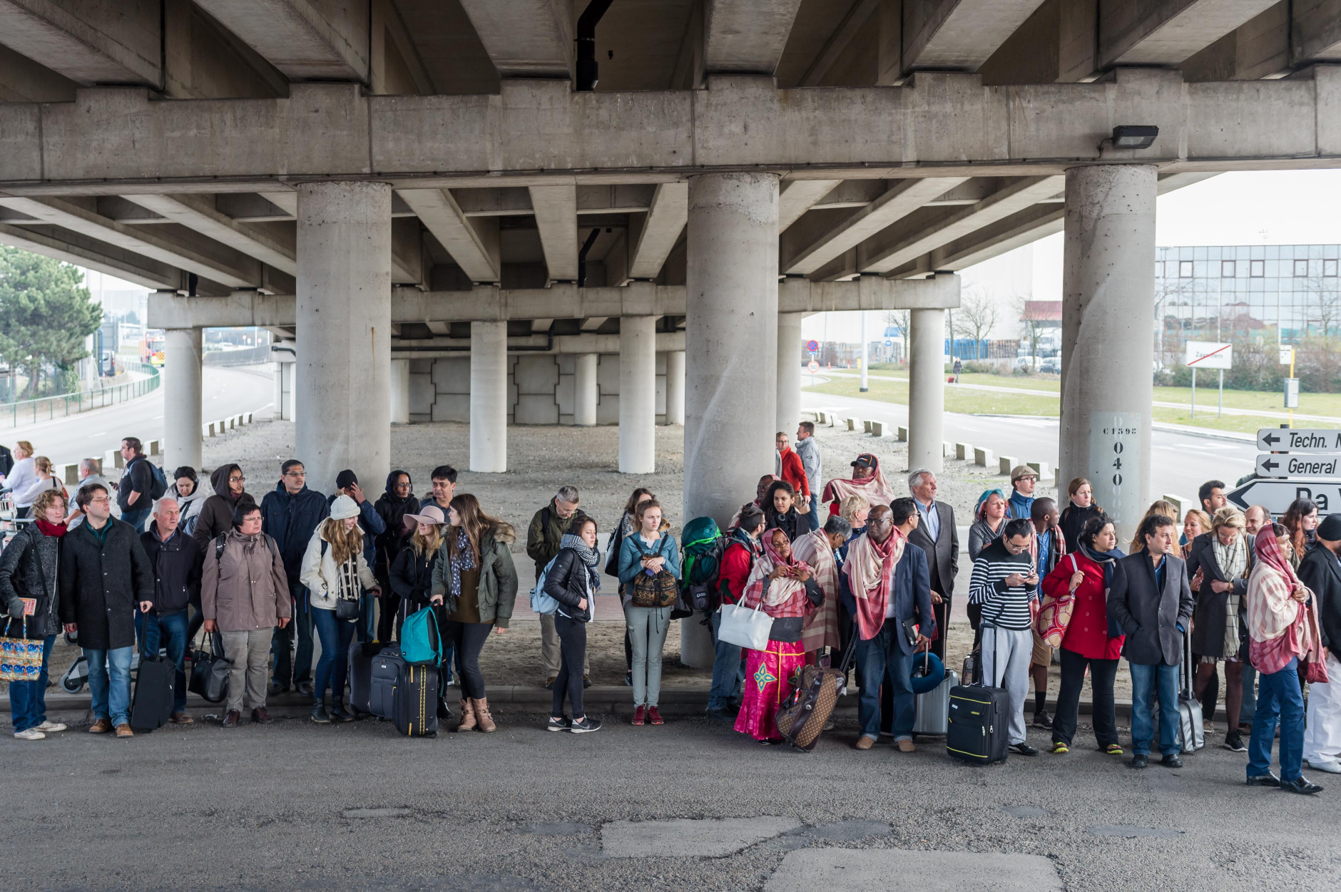 People stand near Brussels airport after being evacuated following  explosions that rocked the facility in Brussels, Belgium, Tuesday March 22, 2016. Authorities locked down the Belgian capital on Tuesday after explosions rocked the Brussels airport and subway system, killing  a number of people and injuring many more. Belgium raised its terror alert to its highest level, diverting arriving planes and trains and ordering people to stay where they were. Airports across Europe tightened security. (AP Photo/Geert Vanden Wijngaert)