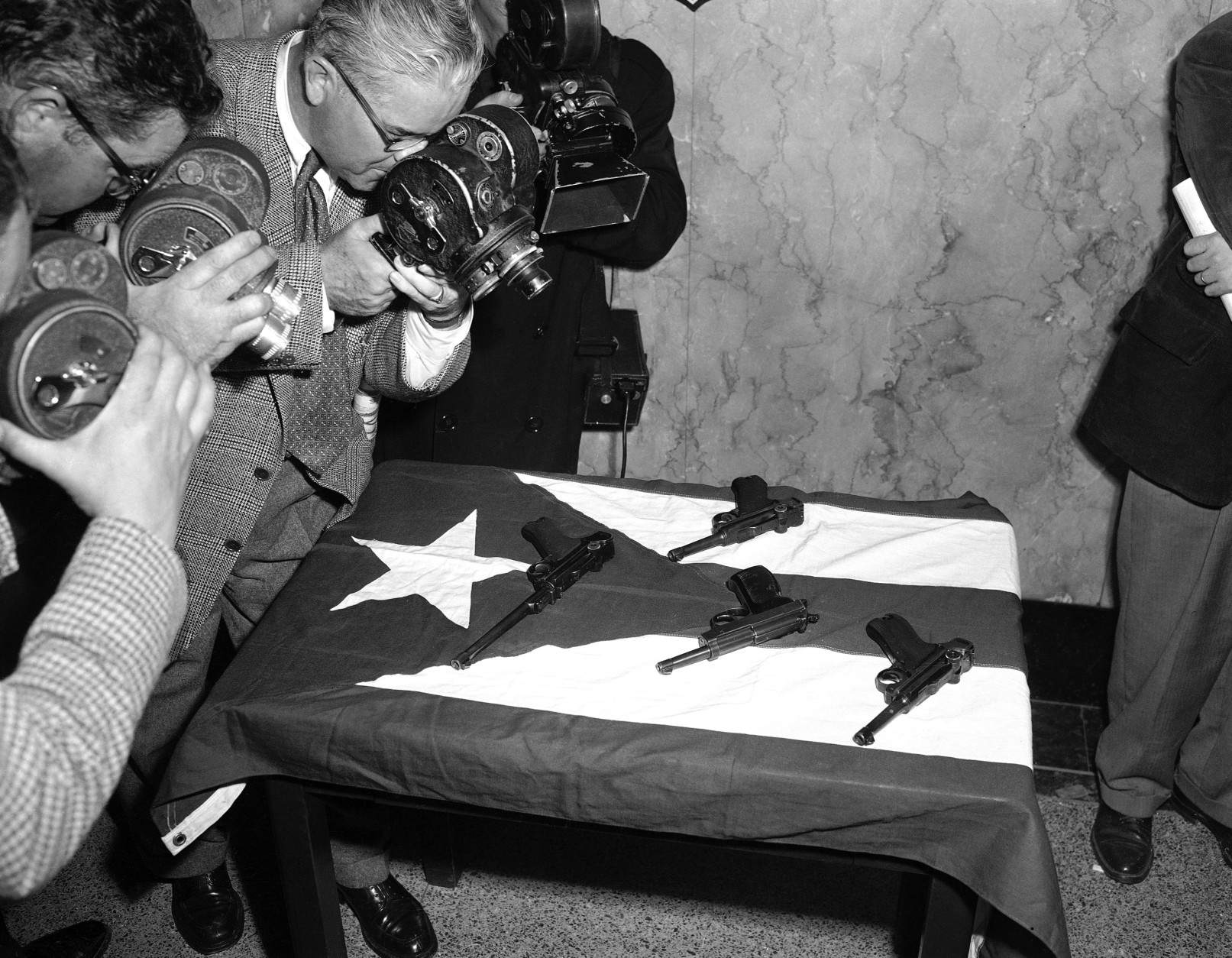 Photographers close in on some souvenirs of a busy day in Congress, spread out at police headquarters on a flag of Puerto Rico, on March 1, 1954. It was a time of routine business, transacted peacefully, in the House chamber when cries of ?Free Puerto Rico? broke the calm, this flag was waved from the spectators gallery and pistol volleys felled five Congressmen. In center foreground is a 38 cal. Automatic. The others are German Lugers. (AP Photo)