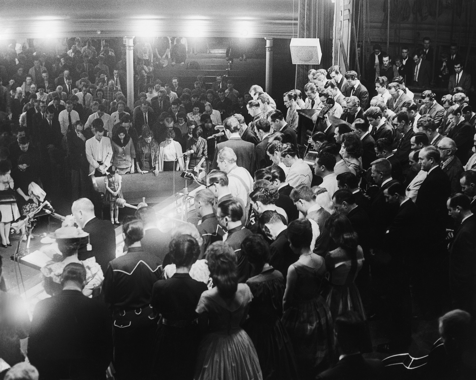 The entire Grand Ole Opry company crowds onstage on March 9, 1963 as Opry Manager Ott Devine (at podium) delivers a message honoring five members killed in accidents last week. It was the same old rollicking show, but onlookers backstage saw through the facade. During Minnie Pearls (at Devines left) performance night, she raced offstage at the end of her act with a typical roar of laughter, then burst into tears in the wings. (AP Photo/Brian Calvert)