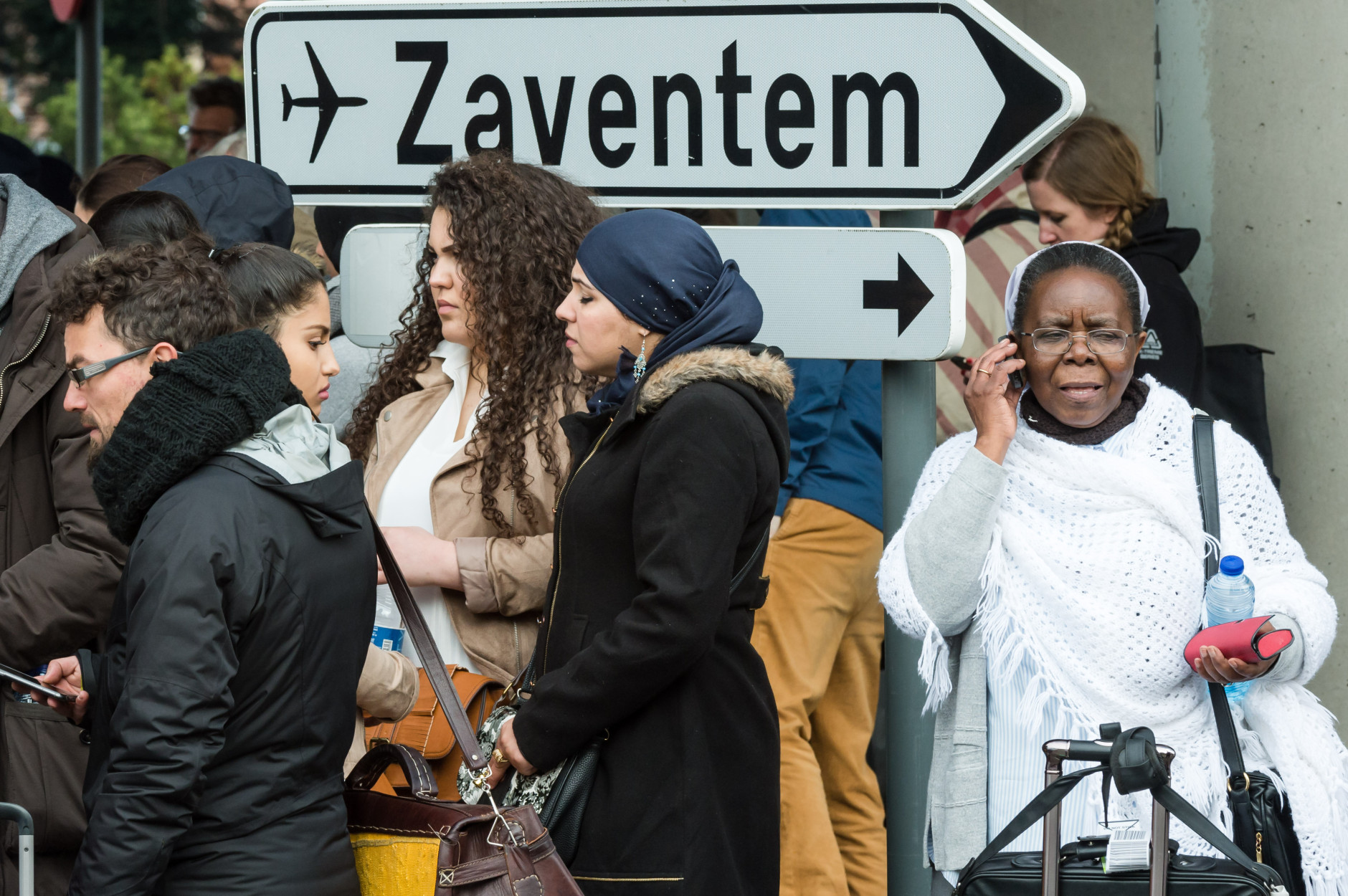 People stand near Brussels airport after being evacuated following  explosions that rocked the facility in Brussels, Belgium, Tuesday March 22, 2016. Authorities locked down the Belgian capital on Tuesday after explosions rocked the Brussels airport and subway system, killing  a number of people and injuring many more. Belgium raised its terror alert to its highest level, diverting arriving planes and trains and ordering people to stay where they were. Airports across Europe tightened security. (AP Photo/Geert Vanden Wijngaert)