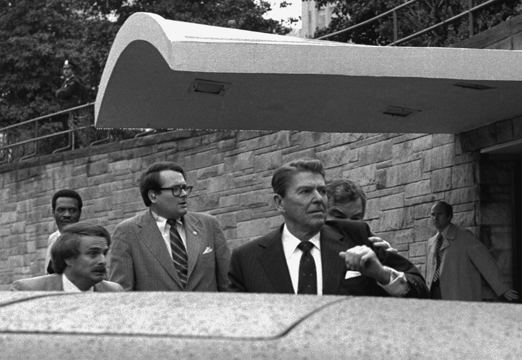 U.S. President Ronald Reagan looks to his left and holds up his left arm as a secret service agent places a hand on his shoulder and pushes the President into his limousine after he was shot leaving a Washington hotel, Monday, March 30, 1981. (AP Photo/Ron Edmonds)
