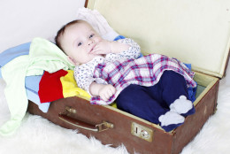 happy baby lying in an old suitcase with clothes