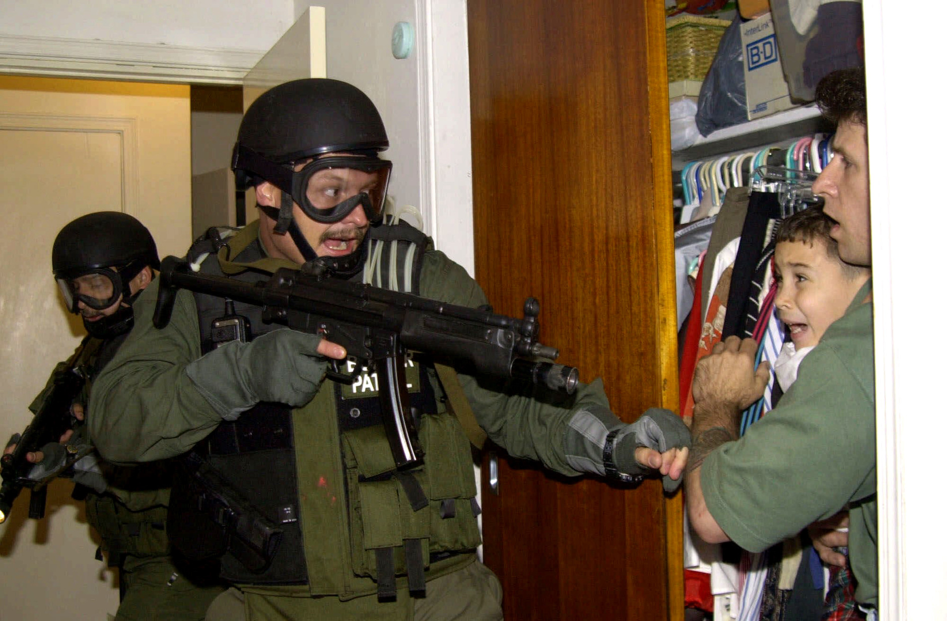 In this third of seven sequential photos, Elian Gonzalez is held in a closet by Donato Dalrymple, one of the two men who rescued the boy from the ocean, right, as government officials search the home of Lazaro Gonzalez for the young boy, early morning, April 22, 2000, in Miami, Florida. Armed federal agents seized Elian Gonzalez from the home of his Miami relatives before dawn, firing tear gas into an angry crowd as they left the scene with the weeping 6-year-old boy. (AP Photo/Alan Diaz)