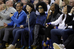 Singer Prince, center, smiles as he watches an NBA basketball game between the Golden State Warriors and the Oklahoma City Thunder Thursday, March 3, 2016, in Oakland, Calif. (AP Photo/Marcio Jose Sanchez)