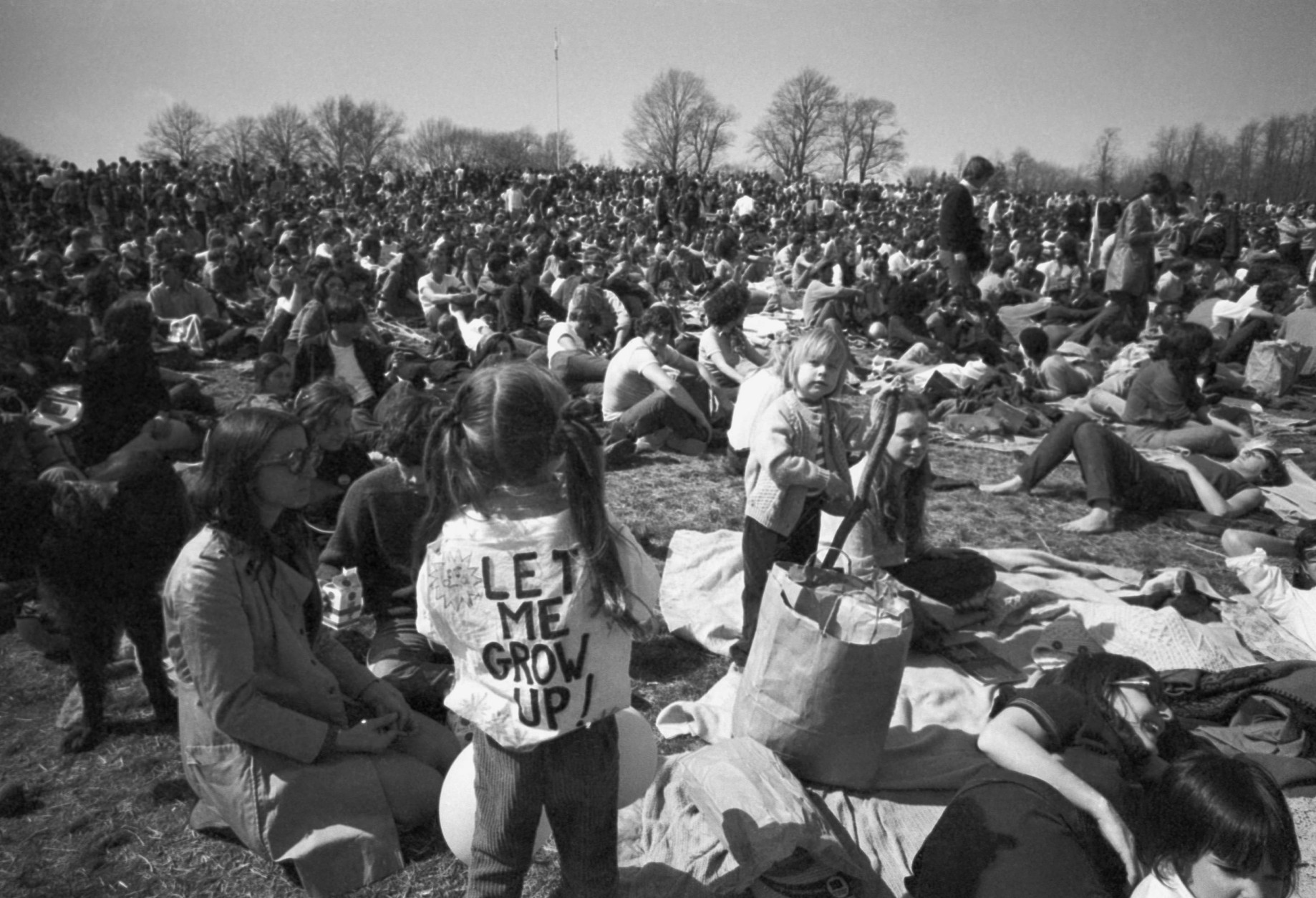 Part of crowd observing Earth Day, including, youngster wearing "Let Me Grow Up:" sign on back relaxes on hilltop in Philadelphia's Fairmount Park Wednesday, April 23, 1970. Crowd made up mostly of young people, was estimated at more than 20,000 persons. (AP Photo)
