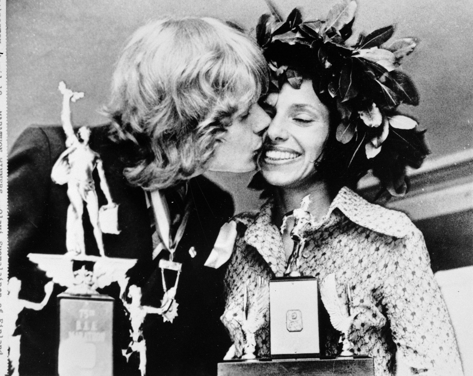 Olavi Suomalainen of Finland, winner of the men's division of the Boston A.A. Marathon April 17, 1972, kisses Nina Kuscsik of Long Island, N.Y., winner of the women's division, at the trophy presentation April 18, 1972. The finish runner won the Hopkinton to Boston marathon 26 mile, 386 yard in two hours, 15 minutes and 30 seconds. Nina's time was three hours, 10 minutes, 58 seconds. (AP Photo)