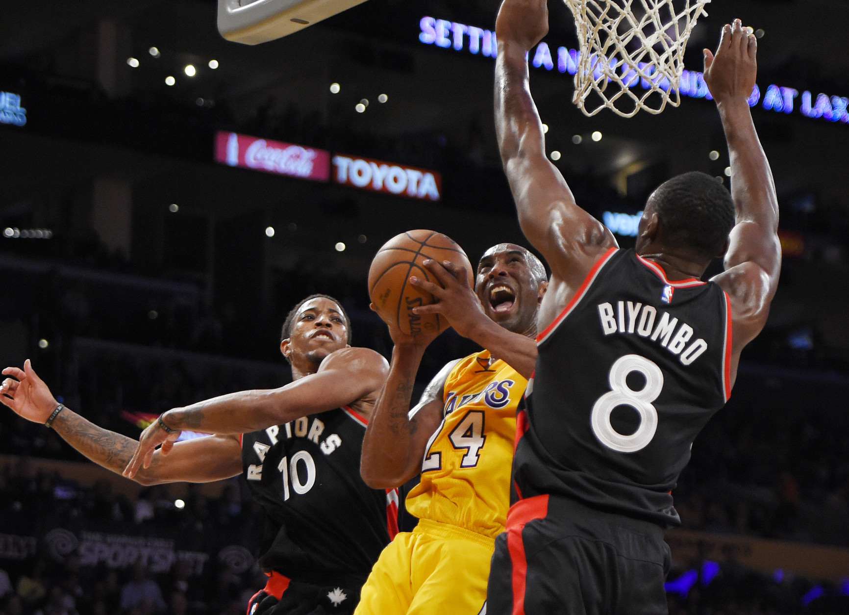 Los Angeles Lakers forward Kobe Bryant, center, shoots as Toronto Raptors guard DeMar DeRozan, left, and forward Bismack Biyombo, of Congo, defend during the second half of an NBA basketball game, Friday, Nov. 20, 2015, in Los Angeles. The Raptors won 102-91. (AP Photo/Mark J. Terrill)