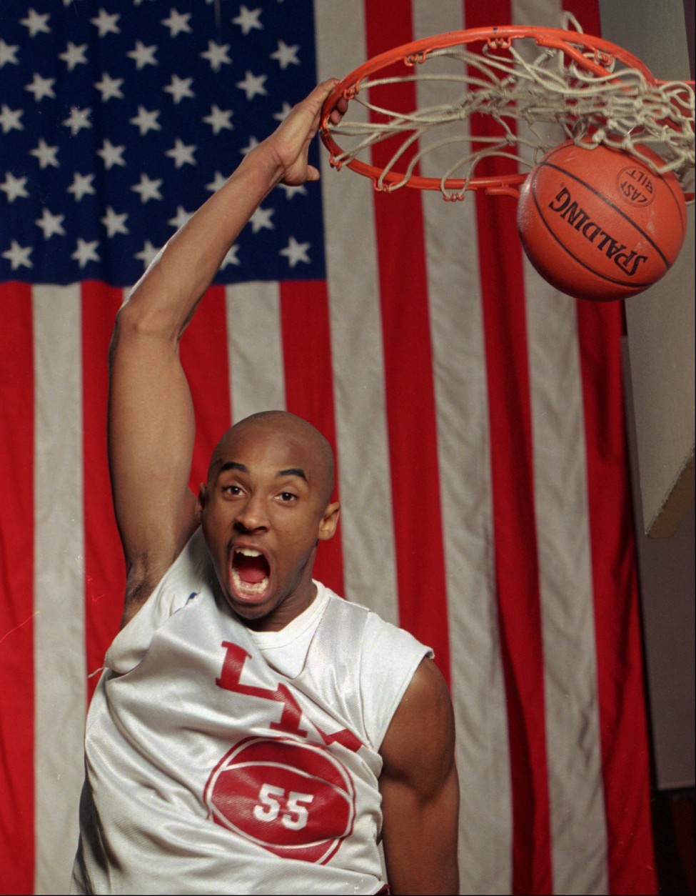 FILE--With a large flag as a backdrop, Kobe Bryant dunks the ball at his Lower Merion, Pa. high school gym during a practice Friday, Jan. 19, 1996. Bryant was chosen by the Charlotte Hornets in the first round of the NBA draft Wednesday June 26, 1996 (AP Photo/rusty kennedy)