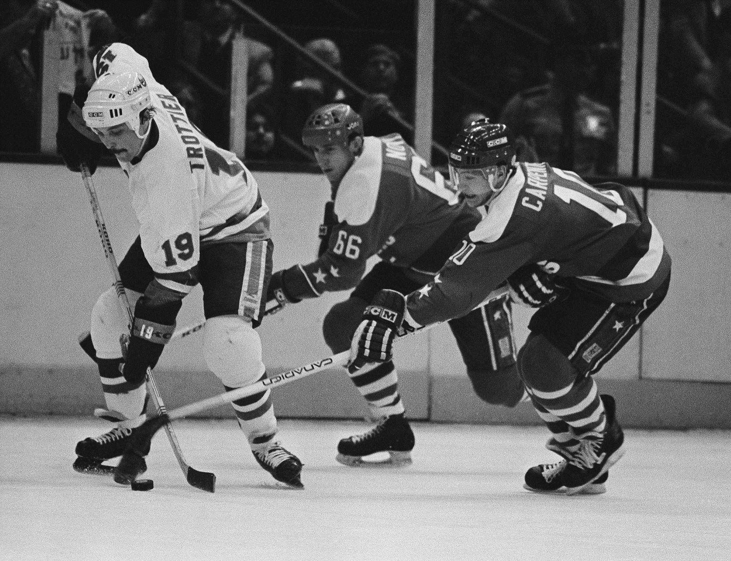 New York Islanders center Bryan Trottier, left, directs the puck against pursuing Washington Capitals in Uniondale, New York, April 7, 1983. Hot on Trottier's heels are Caps Milan Novy, center, and Bob Carpenter in the third period at Nassau Coliseum. Isles beat the Caps 5-2 with Trottier scoring two for the Isles. (AP Photo/Richard Drew)