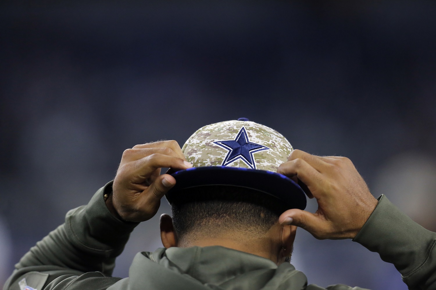 A player puts on a ball cap with the Dallas Cowboys logo in camouflage style before an NFL football game against the Philadelphia Eagles on Sunday, Nov. 8, 2015, in Arlington, Texas. (AP Photo/Brandon Wade)
