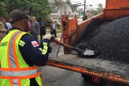 A DDOT worker shovels the warm asphalt from the truck into the waiting potholes. (WTOP/Megan Cloherty)