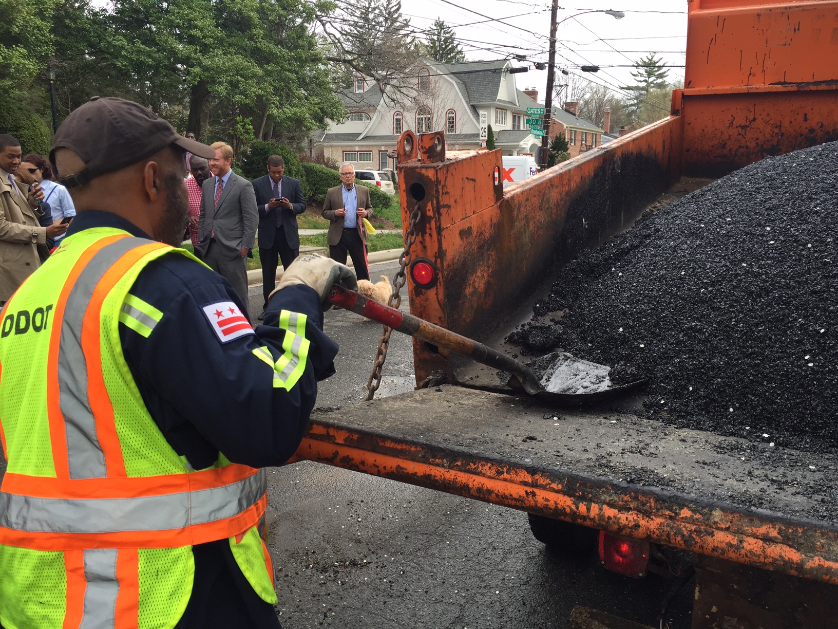 A DDOT worker shovels the warm asphalt from the truck into the waiting potholes. (WTOP/Megan Cloherty)