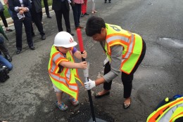 Mayor Muriel Bowser get some help filling a pothole from a neighborhood kid. (WTOP/Megan Cloherty