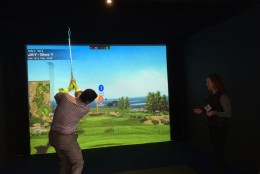 A National Golf Day attendee hits a shot in a simulator in the Rayburn Foyer. (WTOP/Noah Frank)