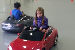 Lila McNamara, 5, test-drives a red Tesla Model S for Kids during a driving event Sunday, May 22, 2016 in Vienna, Va. (WTOP/Kathy Stewart)