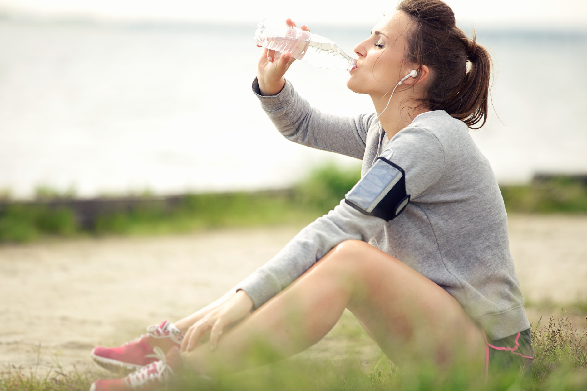 Tired female jogger sitting on the grass and drinking bottled water