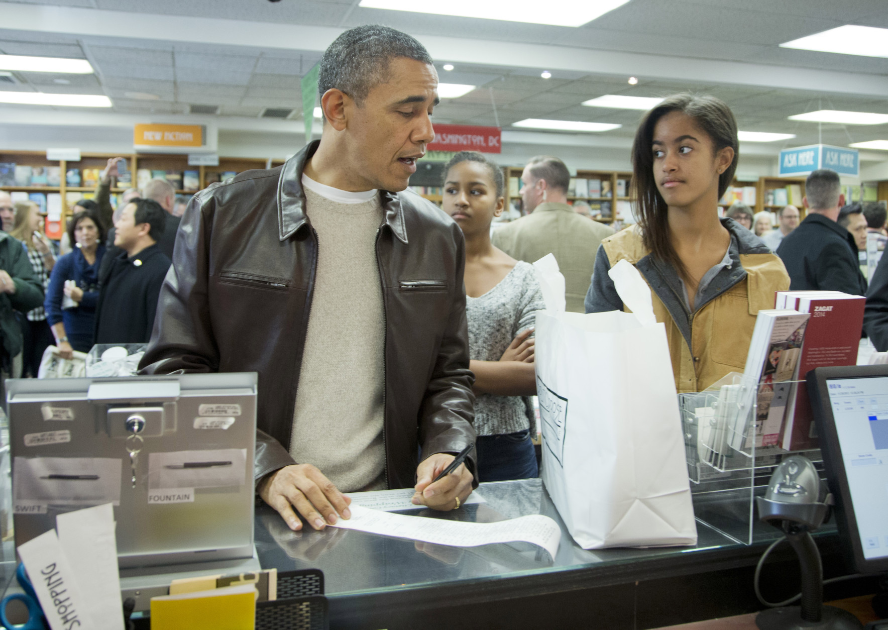 FILE - In this Nov. 30, 2013 file photo, President Barack Obama, with daughters Sasha, center, and Malia, pays for his purchase the the local bookstore Politics and Prose in northwest Washington. President Barack Obamas daughter Malia was just 10 and longing for a promised puppy when her family moved into the White House. Shes marked some of lifes milestones in the past seven years, and another one comes Friday: graduation from high school.  (AP Photo/Manuel Balce Ceneta, File)