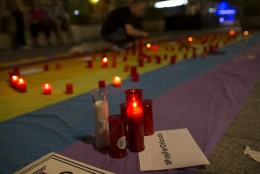 A man lights candles placed on top of a big rainbow flag in solidarity with Florida's shooting attack victims, in Madrid, Spain, Sunday, June 12, 2016. The shooting attack in Orlando, Florida, USA, Sunday, left more than 50 people dead amid a multitude of events celebrating LGBT Pride Month. (AP Photo/Francisco Seco)
