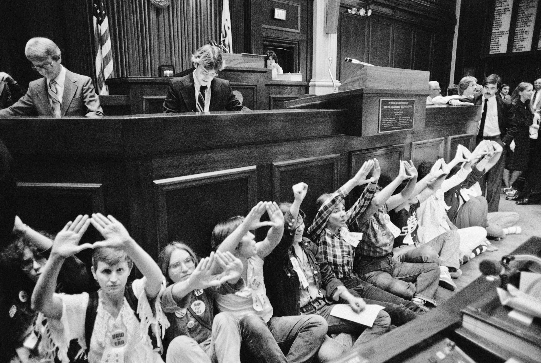 ADVANCE FOR USE MONDAY, JUNE 20, 2016 AND THEREAFTER -FILE - In this Wednesday, June 17, 1982 file photo, women's rights supporters, who earlier chained themselves to the door of the Senate and blocked the door to the governor's office, disrupt a meeting in the Illinois House in Springfield, Ill. Speaker of the House George Ryan dismissed the house after the group seated itself. Demonstrators are giving the sign for female. (AP Photo/Charles Bennett)