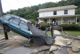 Jay Bennett, left, and step-son Easton Phillips survey the damage to a neighbors car in front of their home damaged by floodwaters as the cleanup begins from severe flooding in White Sulphur Springs, W. Va., Friday, June 24, 2016. A deluge of 9 inches of rain on parts of West Virginia destroyed or damaged more than 100 homes and knocked out power to tens of thousands of homes and businesses. (AP Photo/Steve Helber)