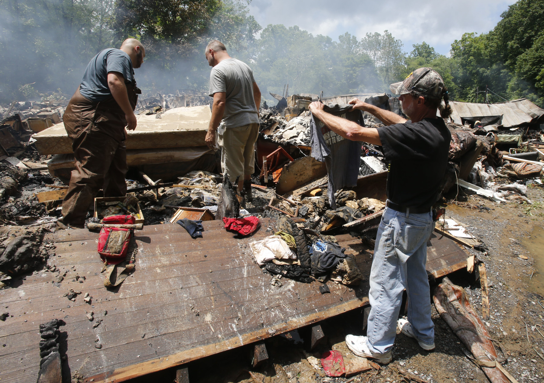 Ron Scott, right, recovers a shirt from the burned remnants of his home that was swept off it's foundation and burned after from severe flooding hit in White Sulphur Springs, W. Va., Friday, June 24, 2016. A deluge of 9 inches of rain on parts of West Virginia destroyed or damaged more than 100 homes and knocked out power to tens of thousands of homes and businesses. (AP Photo/Steve Helber)