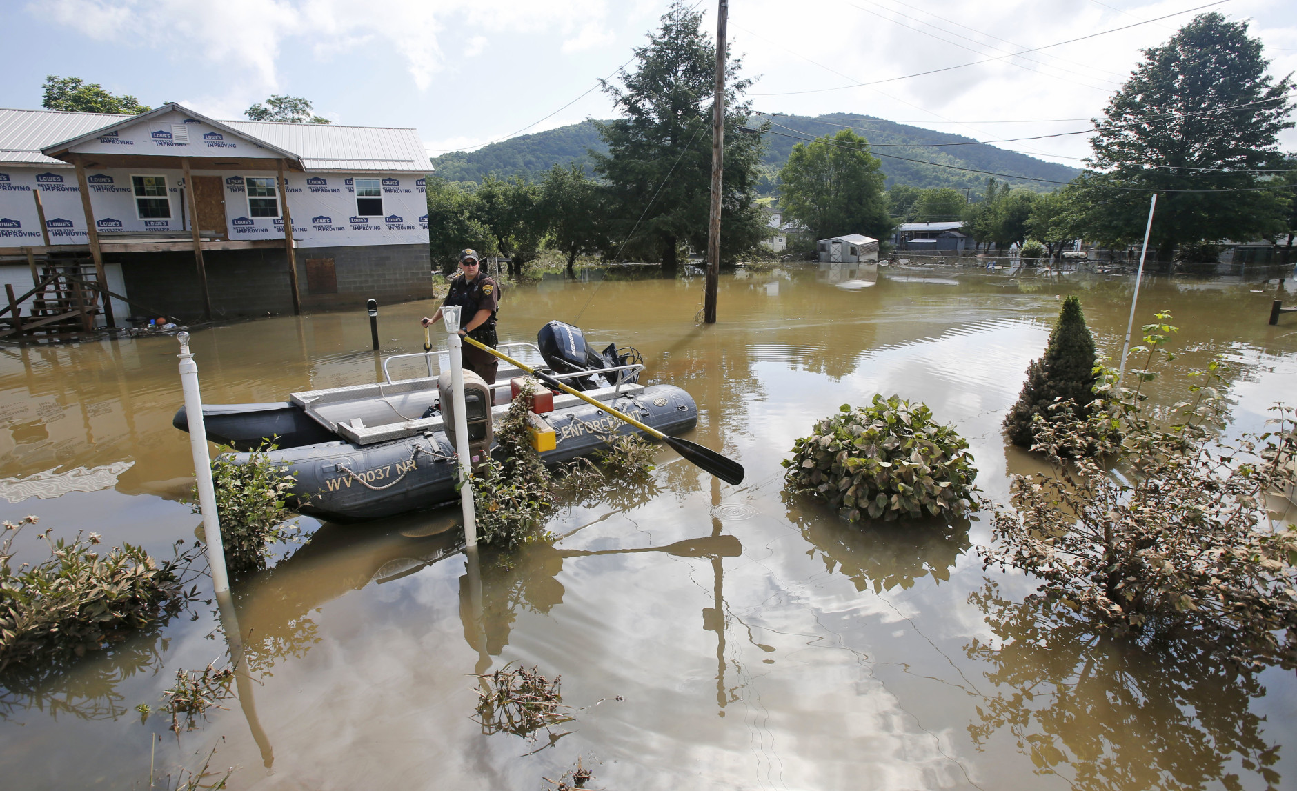 Lt. Dennis Feazell, of the West Virginia Department of Natural Resources, keeps his boat on station as he and a co-worker search flooded homes in Rainelle, W. Va., Saturday, June 25, 2016. Heavy rains that pummeled West Virginia left multiple people dead, and authorities said Saturday that an unknown number of people in the hardest-hit county remained unaccounted for. (AP Photo/Steve Helber)