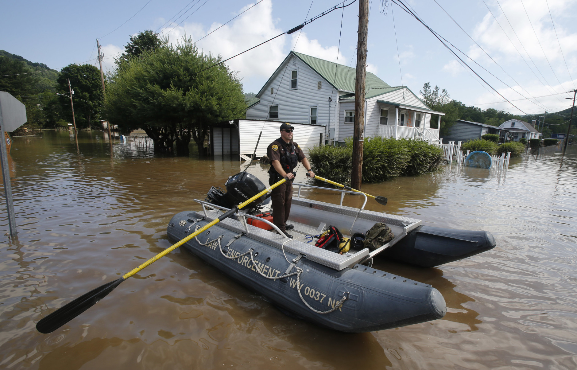 Lt. Dennis Feazell, of the West Virginia Department of Natural Resources, rows his boat as he and a co-worker search flooded homes in Rainelle, W. Va., Saturday, June 25, 2016.  About 32,000 West Virginia homes and businesses remain without power Saturday after severe flooding hit the state. The West Virginia Division of Homeland Security and Emergency Management also said Saturday that more than 60 secondary roads in the state were closed.(AP Photo/Steve Helber)