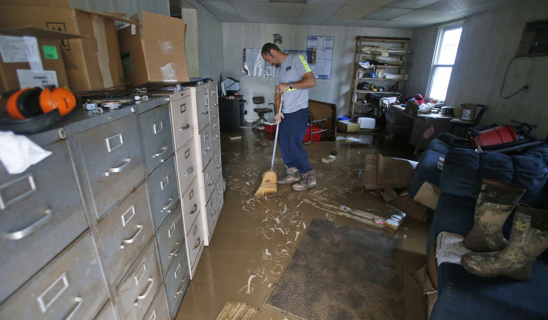 Shane Altzier starts to sweep out the mud from the town utilities office in Rainelle, W. Va., Saturday, June 25, 2016. Heavy rains that pummeled West Virginia left multiple people dead, and authorities said Saturday that an unknown number of people in the hardest-hit county remained unaccounted for .  (AP Photo/Steve Helber)