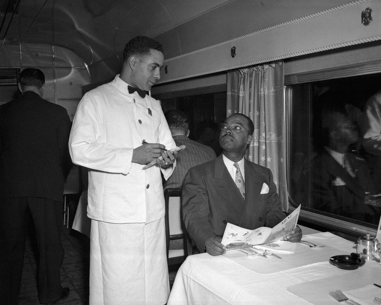 Elmer W. Henderson, seated, a Washington man whose lawsuit was the basis for a Supreme Court decision outlawing segregation in railroad dining cars, orders food from Stanford Peters, a dining car waiter, June 4, 1950.  Henderson, a director of the American Council for Human Rights, went directly from the Supreme Court building to Union Station in Washington to catch the train.  (AP Photo/William J. Smith)