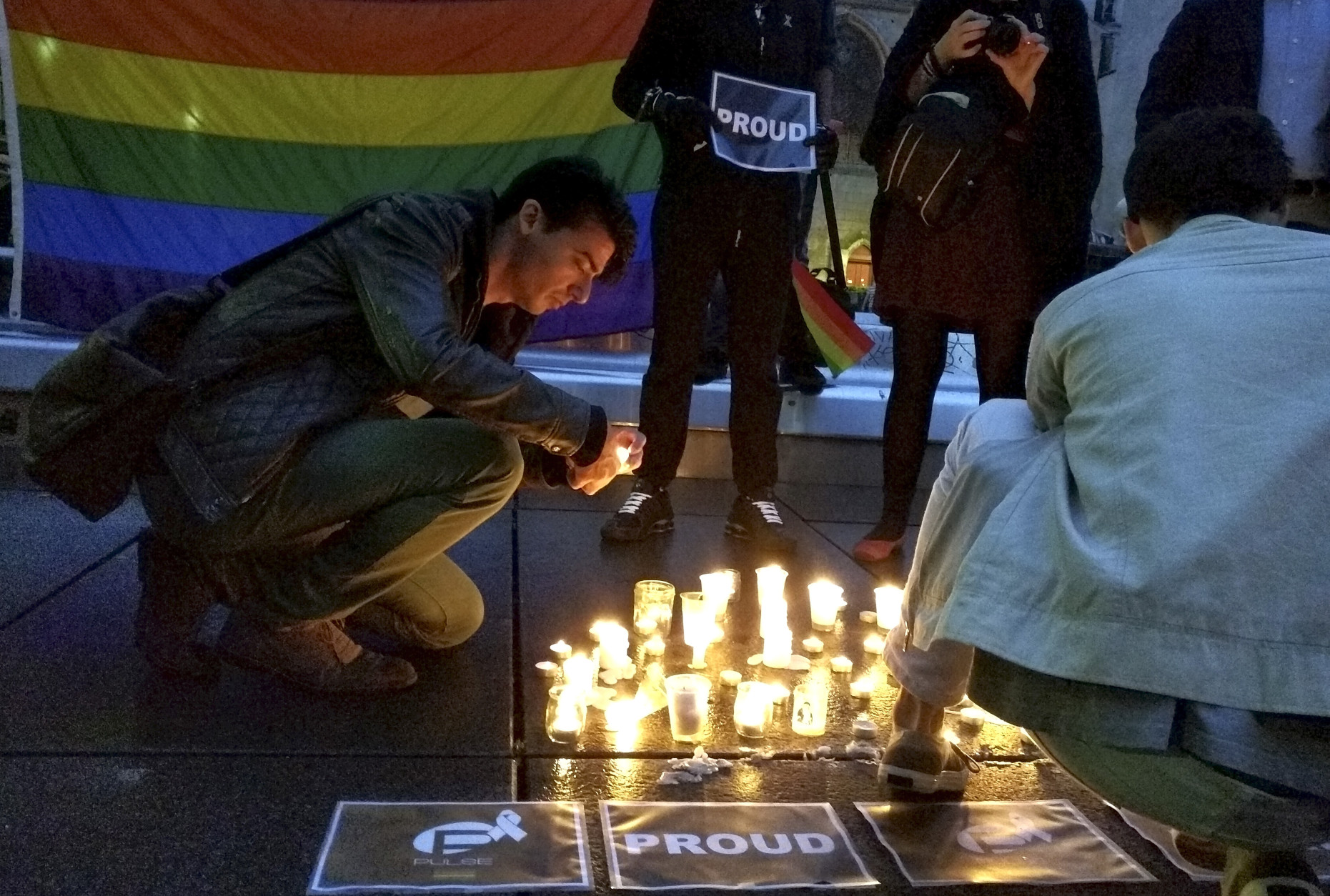 A man lights a candle during a spontaneous  vigil to remember those slain and wounded at an Orlando nightclub, Sunday June 12, 2016 in Paris. Several people were draped in rainbow flags. They lit candles and took pictures as a person in head-to-toe fetish gear held up a sign saying "Proud." (AP Photo/Raphael Satter)