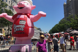 Bonnie Coffey of Maryland waves at the Capitol next to the Famous Dave's pig at the Giant National Capital Barbecue Battle on Saturday in D.C. (WTOP/Kristi King)