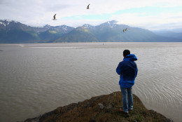 ANCHORAGE, AK - JULY 16:  A man watches from a rock as surfers catch the Bore Tide at Turnagain Arm on July 16, 2014 in Anchorage, Alaska. Alaska's most famous Bore Tide, occurs in a spot on the outside of Anchorage in the lower arm of the Cook Inlet, Turnagain Arm, where wave heights can reach 6-10 feet tall, move at 10-15 mph and the water temperature stays around 40 degrees Fahrenheit. This years Supermoon substantially increased the size of the normal wave and made it a destination for surfers.  (Photo by Streeter Lecka/Getty Images)
