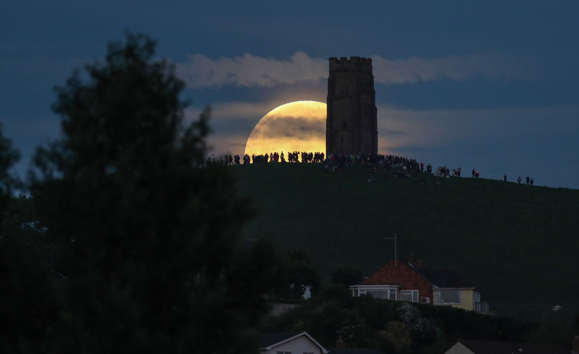 A full moon rises behind Glastonbury Tor as people gather to celebrate the summer solstice on June 20, 2016 in Somerset, England. Tonight's strawberry moon, a name given to the full moon in June by Native Americans because it marks the beginning of strawberry picking season, last occurred on the solstice on June 22, 1967 and it will not happen again on the summer solstice for another 46 years until June 21, 2062.  (Photo by Matt Cardy/Getty Images)