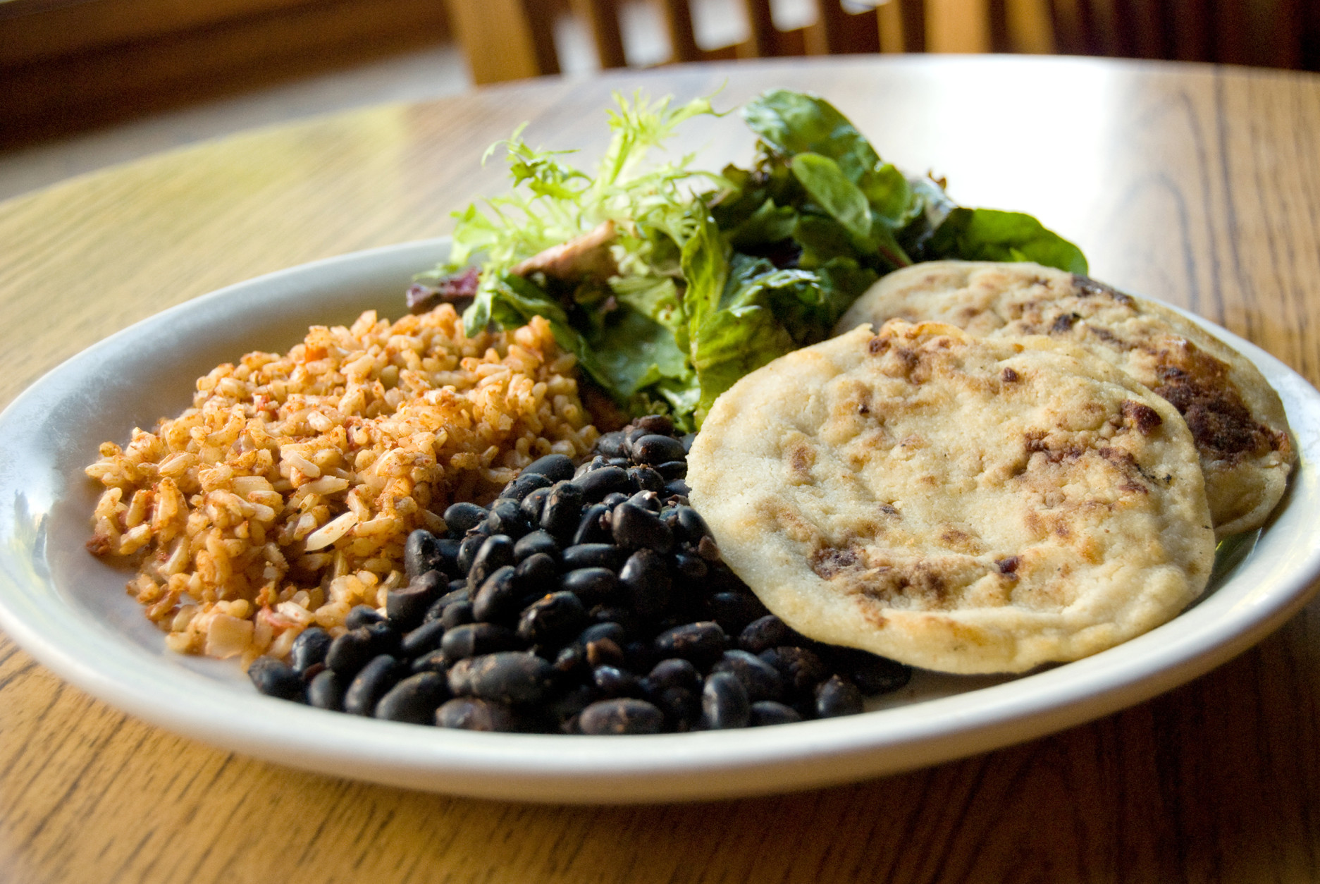 Papusas (stuffed tortillas) served with black beans, rice, and a microgreen salad.