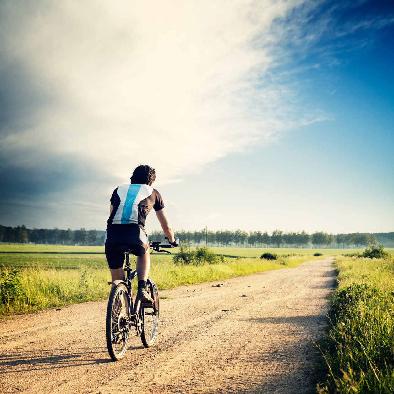 Cyclist Riding a Bike on the Country Road. Rear View. Summer Nature Background. Healthy Lifestyle Concept. Instagram Styled Toned and Filtered Photo. Copy Space.