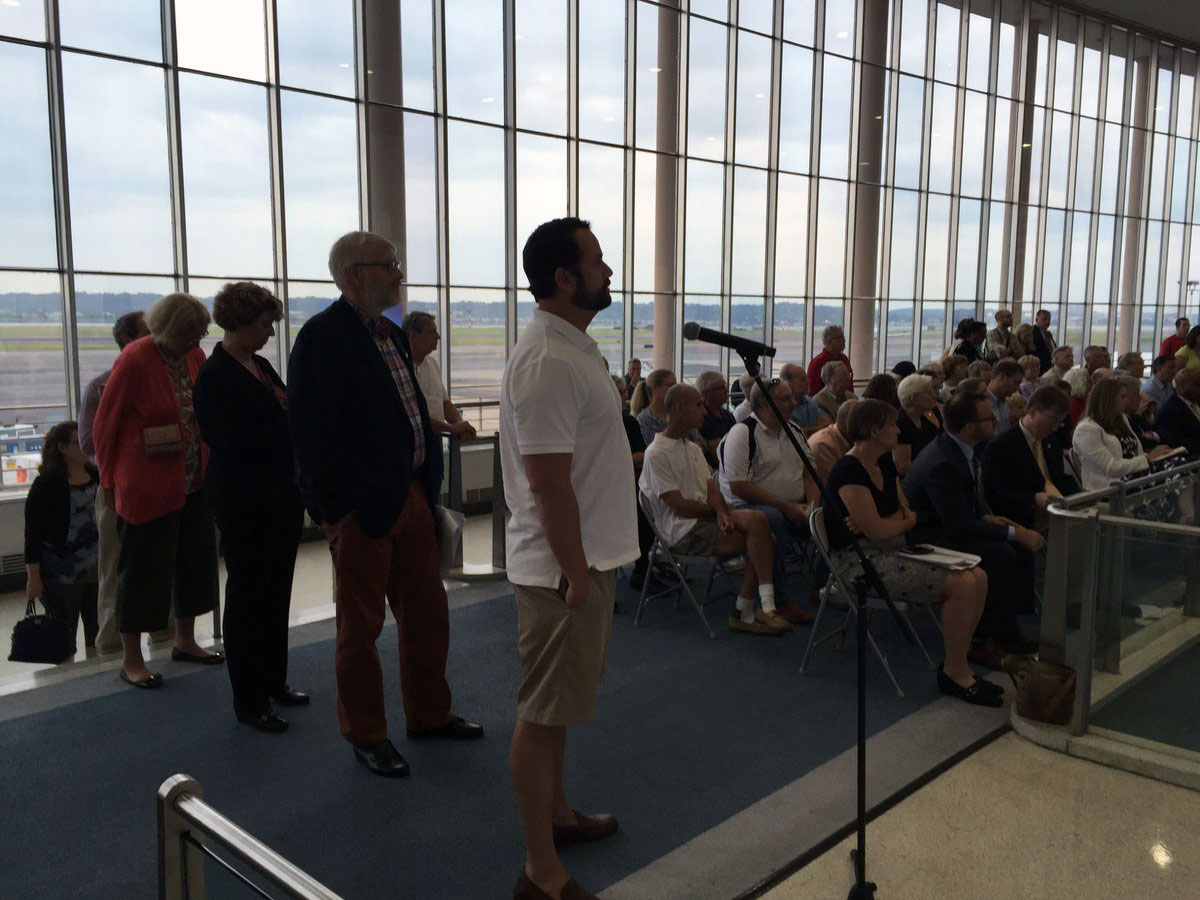Residents line up to comment about airport noise as planes noisily take off behind them at Reagan National Airport. (WTOP/Michelle Basch)