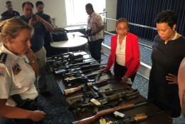 At a news conference Thursday, D.C. police Chief Cathy Lanier, D.C. Congressional Delegate Eleanor Holmes Norton and D.C. Mayor Muriel Bowser examine just a few of the assault rifles removed from city streets in recent weeks. (WTOP/Kristi King)