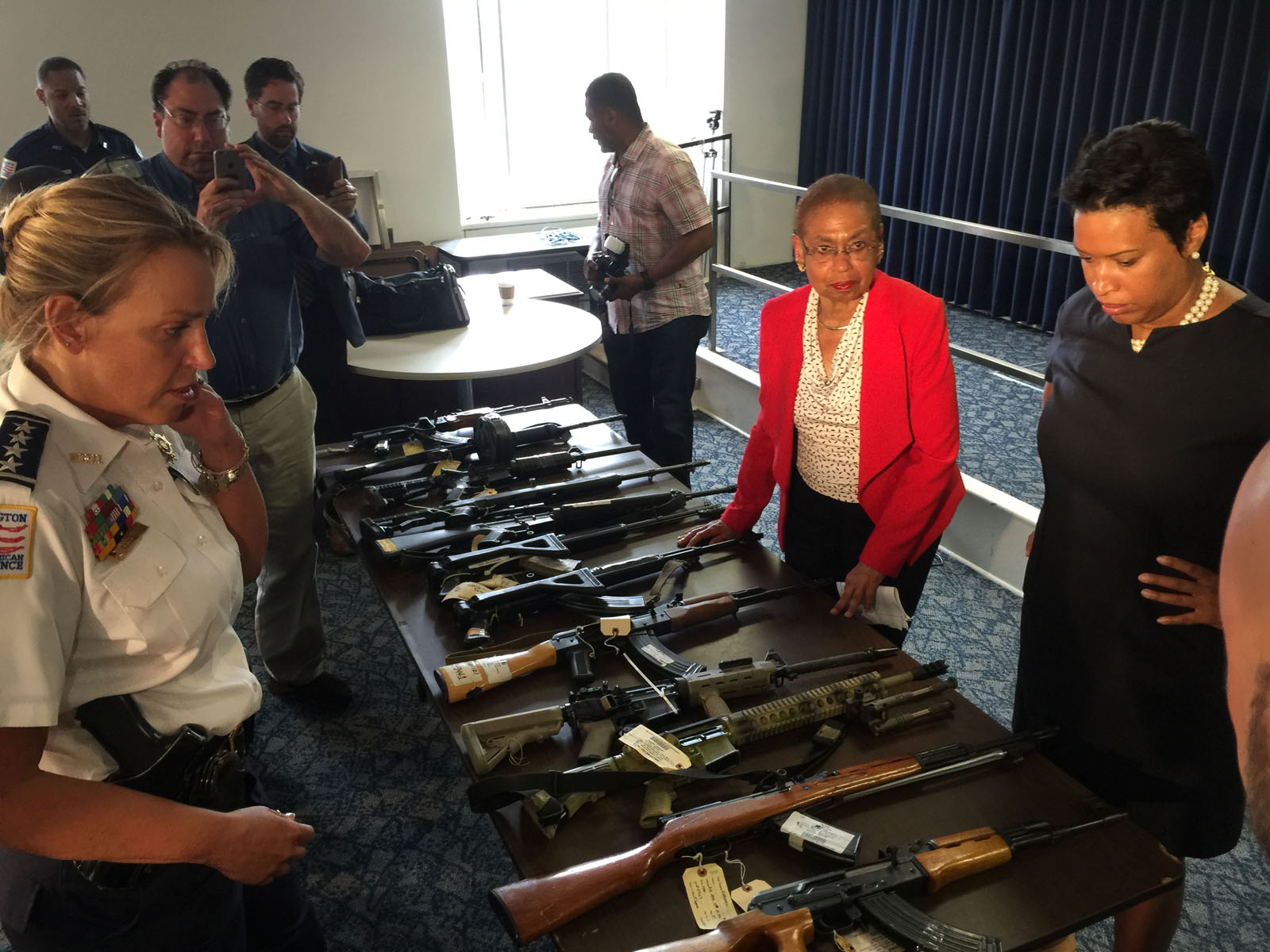 At a news conference Thursday, D.C. police Chief Cathy Lanier, D.C. Congressional Delegate Eleanor Holmes Norton and D.C. Mayor Muriel Bowser examine just a few of the assault rifles removed from city streets in recent weeks. (WTOP/Kristi King)
