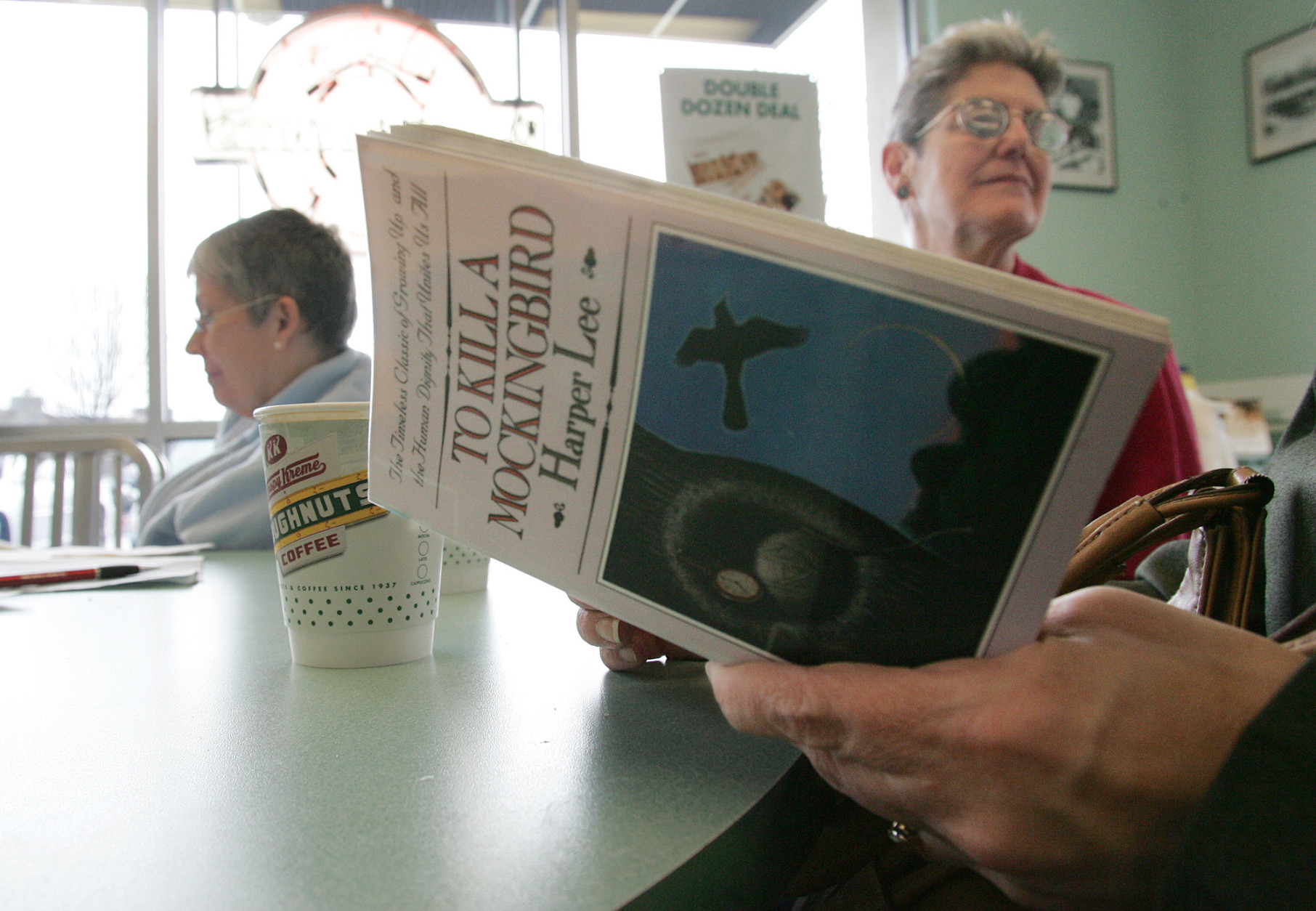 Sandra Lindley, right and Lydia Kuhn behind listens to a reader at the Krispy Kreme shop Monday, March 6, 2006, in Fresno, Calif. Kuhn and others like her spent the morning reading "To Kill a Mockingbird," as part of The National Endowment for the Arts effort to get American's to read more. The program helped kick off a month's worth of programs meant to take the classic novel where the readers are; doughnut shops, retirement homes, downtown bars, museums and yes, even libraries.(AP Photo/Gary Kazanjian)