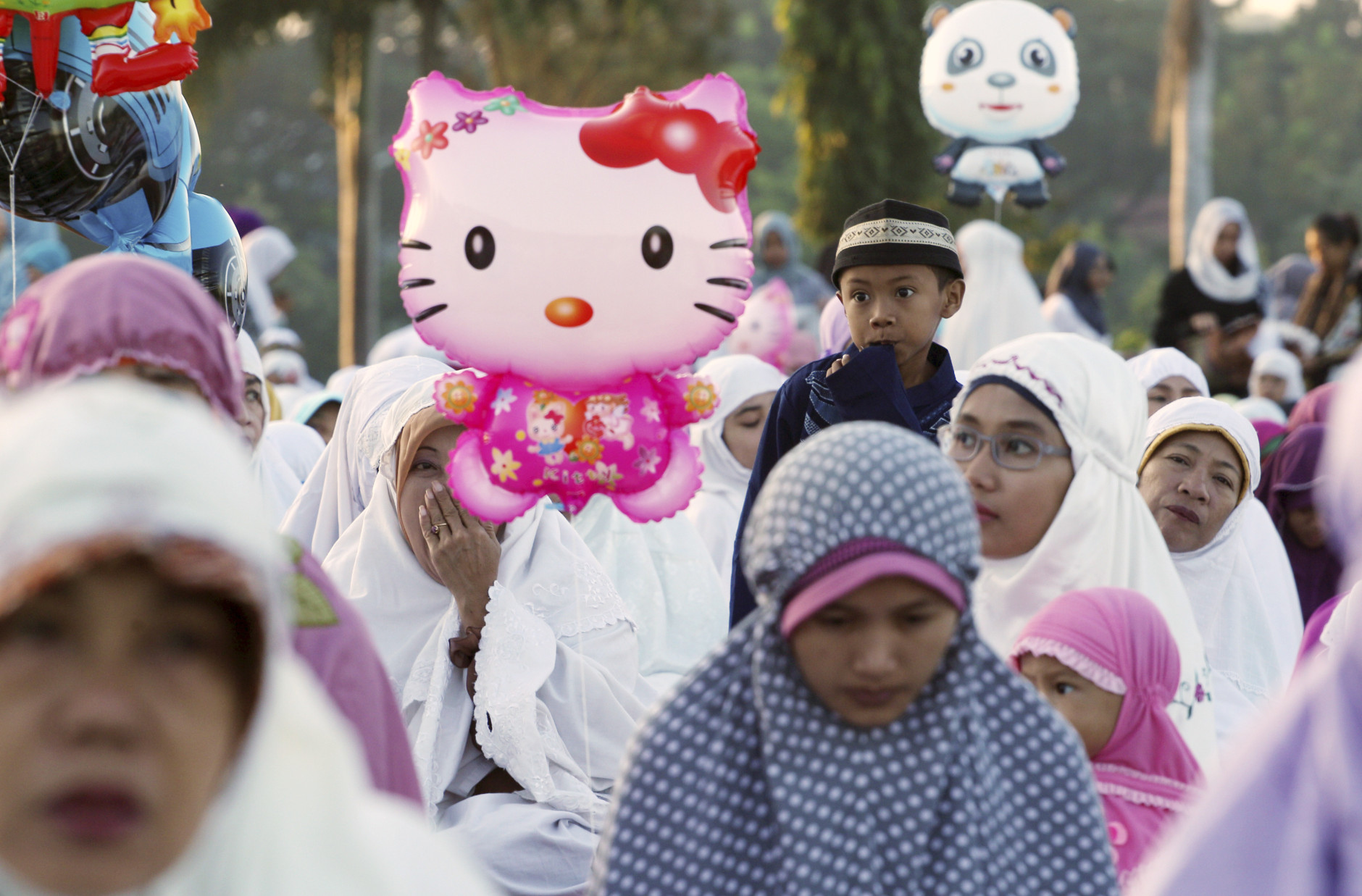 Muslim women attend an Eid al-Fitr prayer, with a  balloon of cartoon character "Hello Kitty" floating, to mark the end of the holy fasting month of Ramadan in Bali, Indonesia, Wednesday, July 6, 2016.(AP Photo/Firdia Lisnawati)