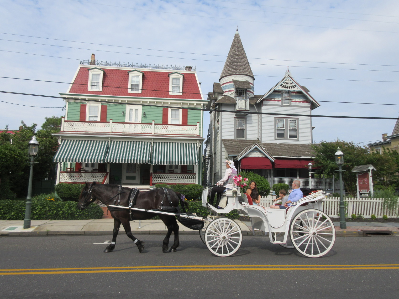 This June 26, 2015 photo shows visitors taking a horse carriage tour of Cape May, N.J. The city's hundreds of Victorian homes constitute what the National Historic Landmarks program calls one of the largest collections of 19th century frame buildings in the United States. Their gables, towers, domes, arched windows and inviting front porches, often trimmed in bright colors, create charming and whimsical streetscapes.  (AP Photo/Beth J. Harpaz)