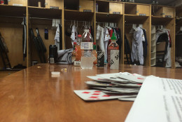 A clubhouse table littered with various beverages, hot sauces a deck of cards and a copy of a chapel sermon after the team has departed for their next road trip. (WTOP/Noah Frank)