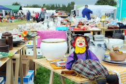 It's a typical impression of Flea Market at Havelberg (Saxony-Anhalt, Germany), that takes place every year around the first September Weekend. In front tables with colorful clown marionette for puppet show and dishware. in background group of visitors taking a look on products. dark clouds on shy. in background German words "jedes Teil nur"... its English every item just...