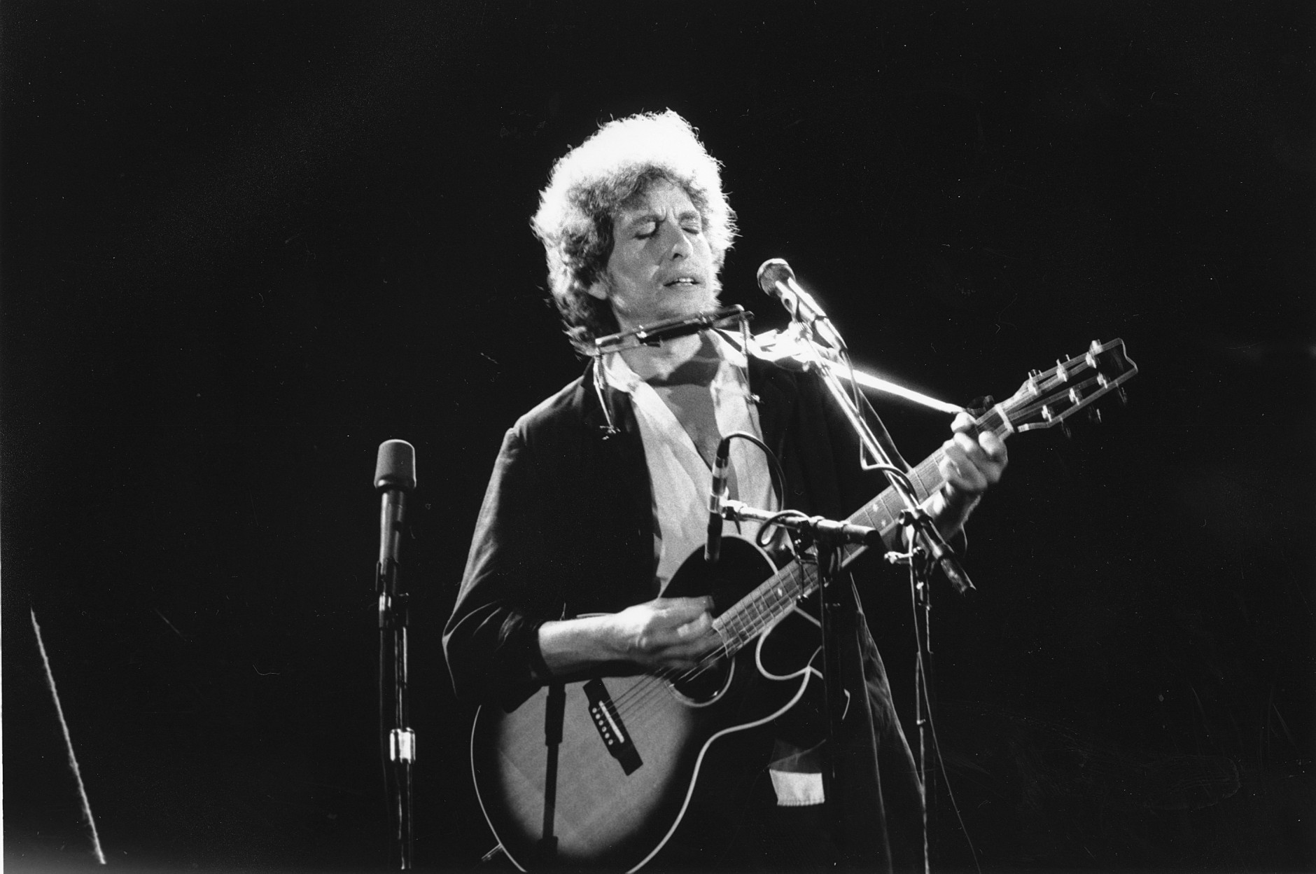 This is an undated photo of singer-songwriter Bob Dylan as he plays his acoustic guitar with his harmonica at an unknown location.  (AP Photo)