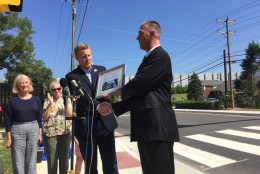 Virginia Delegate Vivian Watts (39th District), looks on as Fairfax County Supervisor Jeff McKay (Lee District) is presented a plaque by Fairfax County Department of Transportation Director Tom Biesiadny noting the installation of the county's first HAWK pedestrian-oriented traffic signal. (WTOP/Kristi King)