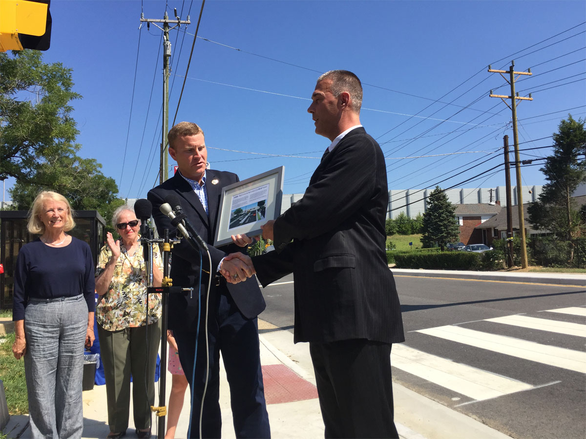 Virginia Delegate Vivian Watts (39th District), looks on as Fairfax County Supervisor Jeff McKay (Lee District) is presented a plaque by Fairfax County Department of Transportation Director Tom Biesiadny noting the installation of the county's first HAWK pedestrian-oriented traffic signal. (WTOP/Kristi King)
