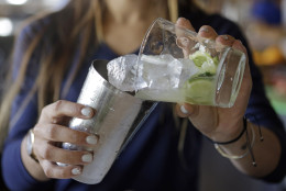 In this photo taken May 10, 2016, bartender Rafaella Demelo, adds the sugar, 1.5 ounces of Leblon and a half lime cut in cubes with ice to the shaker as she goes through the final steps preparing a Caipirinha at Bulla, a Spanish gastro bar in Coral Gables, Fla. The caipirinha's sweet, tropical flavors may resemble a mojito, it's closer in spirit to a margarita, according to Luttman. As the caipirinha has gained popularity in many bars, particularly those that hosted viewing parties for Brazil's World Cup two years ago, some bartenders now mix variations of the cocktail with vodka or sake and add strawberries, oranges or other fruits.(AP Photo/Alan Diaz)
