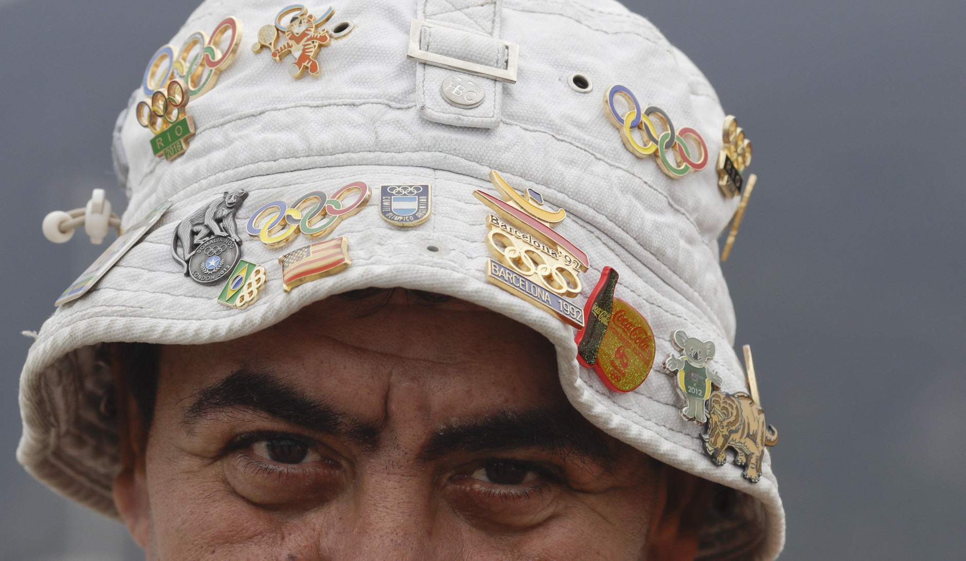 A man wearing a hat with pins poses for a picture outside the Olympic village ahead of the 2016 Summer Olympics in Rio de Janeiro, Brazil, Wednesday, Aug. 3, 2016. The Games opening ceremony is on Friday.(AP Photo/Natacha Pisarenko)