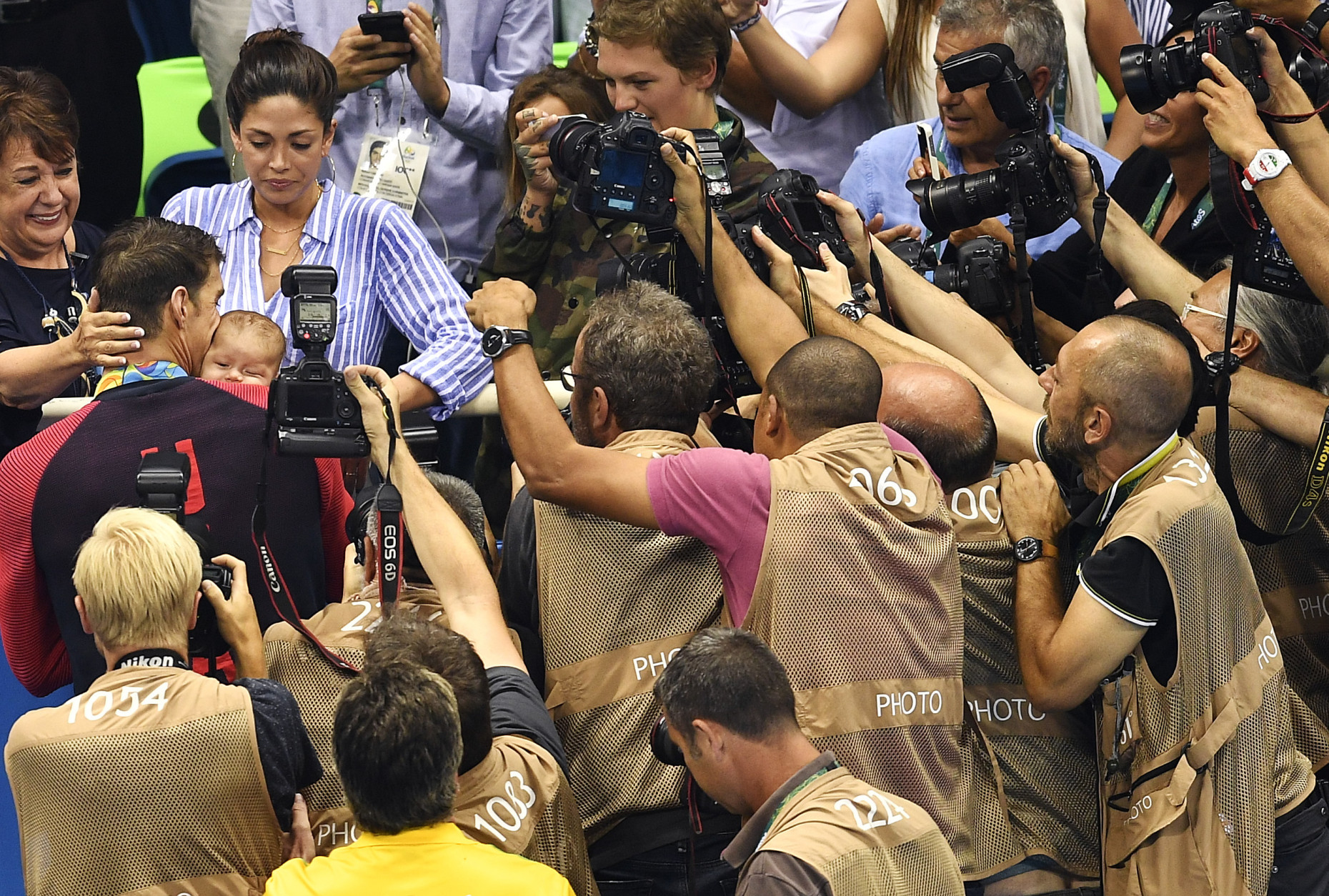 United States' Michael Phelps is surrounded by media as he kisses his son Boomer, held by his fiancee Nicole Johnson, second left, after winning the gold medal in the men's 200-meter butterfly final during the swimming competitions at the 2016 Summer Olympics, Tuesday, Aug. 9, 2016, in Rio de Janeiro, Brazil. (AP Photo/Martin Meissner)