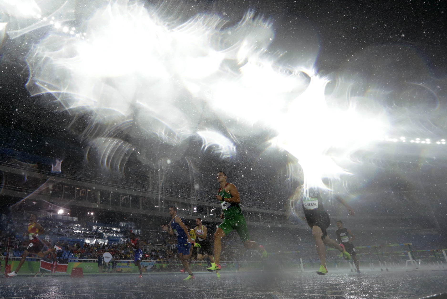 Hungary's Balazs Baji, center, and Canada's Johnathan Cabral compete in a men's 110-meter hurdles heat during heavy rain at the athletics competitions of the 2016 Summer Olympics at the Olympic stadium in Rio de Janeiro, Brazil, Monday, Aug. 15, 2016. (AP Photo/Matt Slocum)